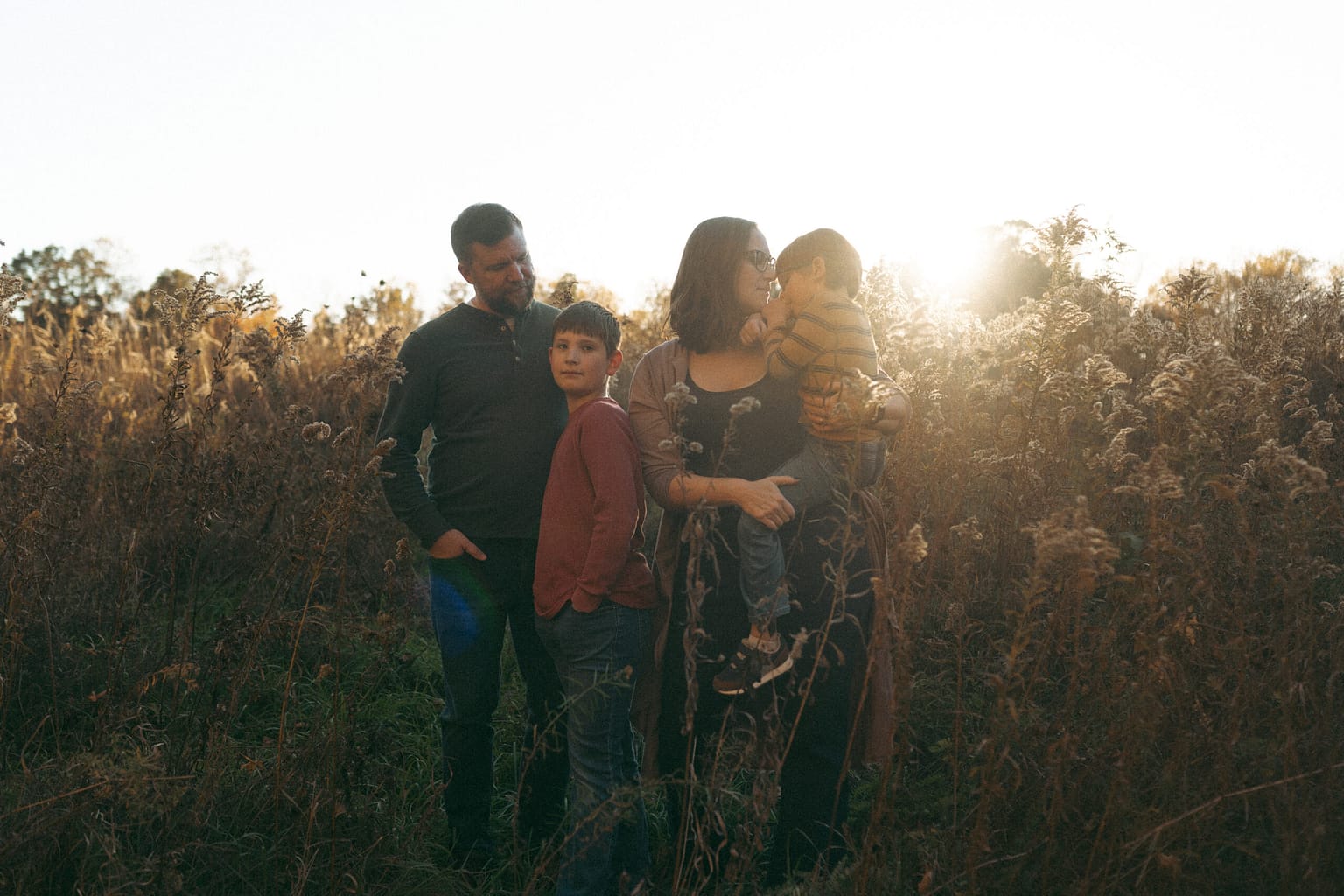 family of four with mom and dad and two young boys standing in a field