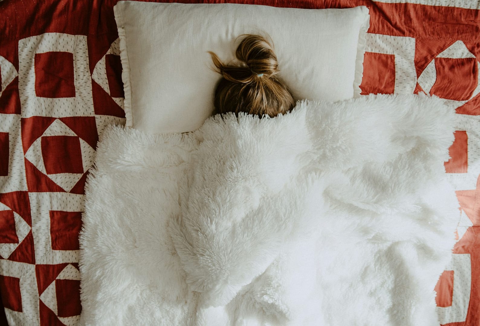 white fur textile on red and white textile with woman hiding under covers