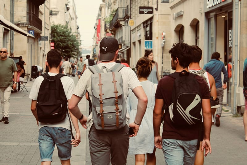 a group of teens and young adults with backpacks are walking down a street in a european city